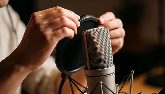 Hands adjusting condenser microphone pop filter for podcasting and voiceover recording