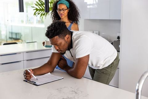 African american man signing document on kitchen countertop while partner observing