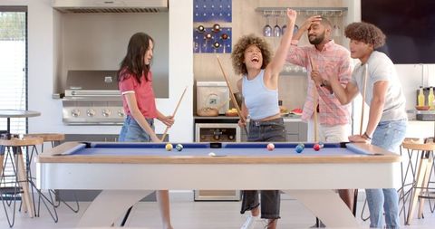 Diverse group of friends celebrating and playing pool inside modern home