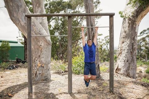 Man hanging on outdoor pull-up bar in woodland area