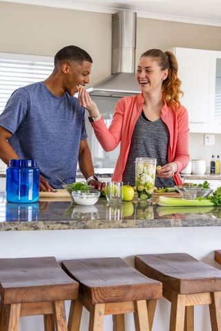 Couple preparing healthy green smoothie and feeding each other in modern kitchen
