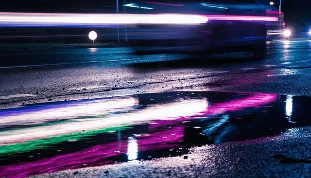 Neon Lights Streaking and Reflecting on Wet Urban Street Puddle, Motion-Blur Traffic