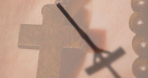 Wooden cross pendant casting crucifix shadow over rosary beads in warm macro closeup