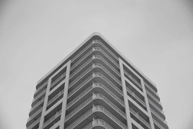 This image captures the geometric symmetry of a modern high-rise building viewed from below. With its clean lines and urban appeal, it can be used to depict city living, minimalist architectural design, and contemporary lifestyle. Ideal for advertisements related to real estate, architecture firms, urban development projects, and modern living concepts.