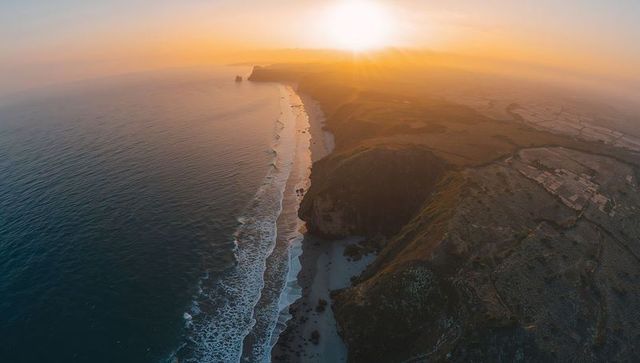 Golden sunset lighting rugged coastal cliffs and long sandy beach from aerial viewpoint