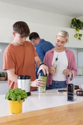 Teen securing personal blender cup while parents preparing healthy meal in modern kitchen