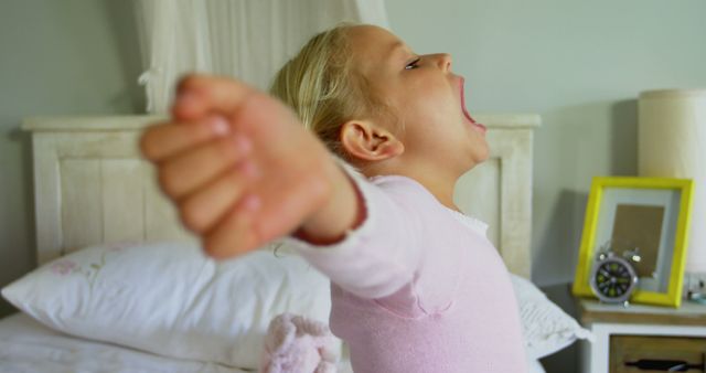 Blonde girl yawning and stretching in her bed, starting her morning routine. Suitable for themes of sleep, morning habits, childhood, and family life. Can be used in articles or promotions about children's health, sleep hygiene, and establishing daily routines.