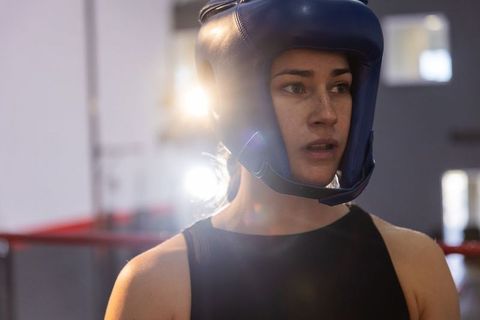 Focused female boxer pausing in ring wearing blue headguard and black training top