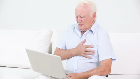 Elderly Man Experiencing Discomfort While Using Laptop at Home