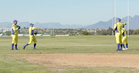 Diverse male teammates throwing on suburban baseball field in yellow uniforms under sunny sky