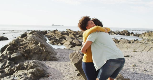 Friends embracing at a rocky beach with an ocean backdrop, expressing joy and happiness. Can be used for themes related to friendship, bonding, nature trips, vacations, emotional connections, or beach activities.