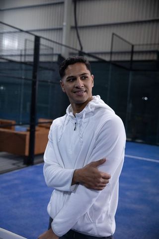 Asian athlete standing on indoor blue court wearing white hoodie arms folded and smiling