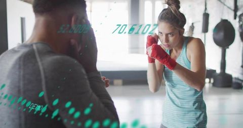 Female boxer sparring with trainer in bright gym wearing turquoise tank and red hand wraps