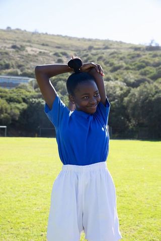 Young Girl Stretching on Soccer Field in Blue Shirt