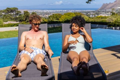 Interracial couple sunbathing on deck loungers beside infinity pool with ocean view