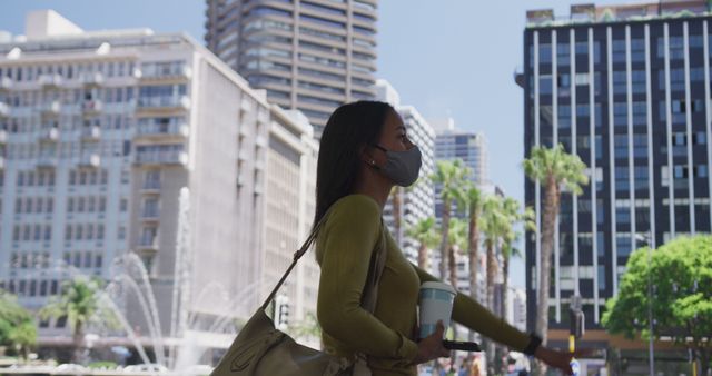 Urban woman in face mask holding coffee cup walking in city during daytime - Download Free Stock Images Pikwizard.com