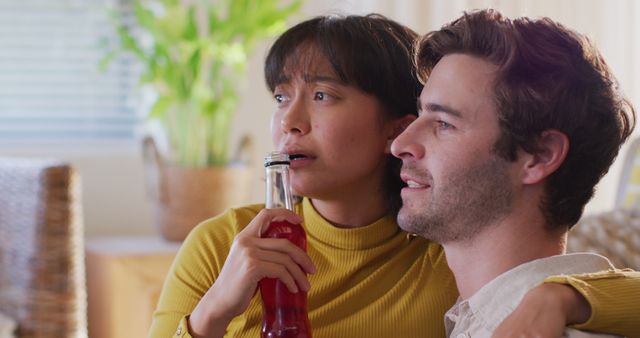 Image of happy diverse couple drinking beer and talking in living room. Love, relationship and spending quality time together concept.