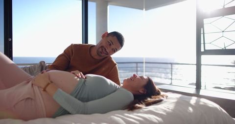 Expectant couple relaxing and enjoying ocean view in bedroom