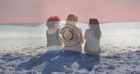Three friends sitting on beach watching ocean with paraguay flag overlay and emblem
