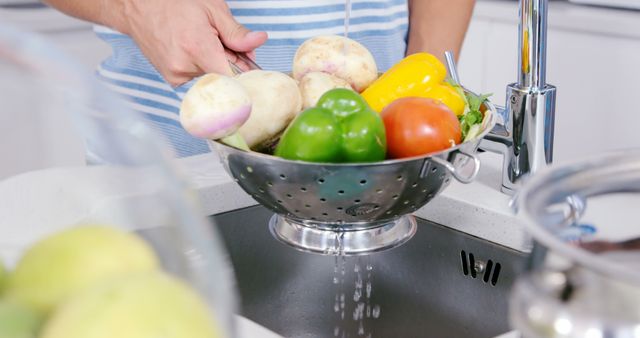 Person washing fresh vegetables, including bell peppers, tomatoes, turnips using a metal colander in a kitchen sink. Ideal for healthy eating, home cooking, organic food, kitchen hygiene, and lifestyle blogs or websites.