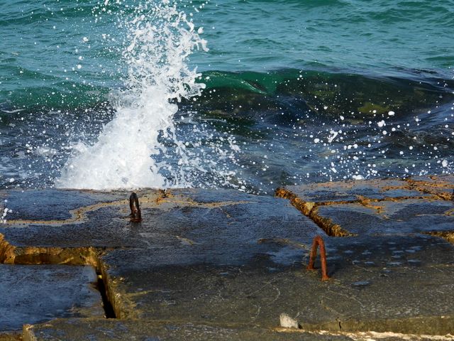 Blue ocean waves crashing against concrete pier with rusty metal hooks, splashing water. Ideal for nature scenes, coastal environments, industrial themes, or backgrounds focused on sea and water activity.