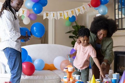 Parents preparing colorful home birthday party with child, balloons and cupcakes