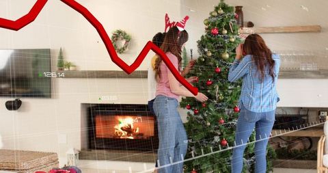 Three women decorating christmas tree while falling stock market graph overlays scene