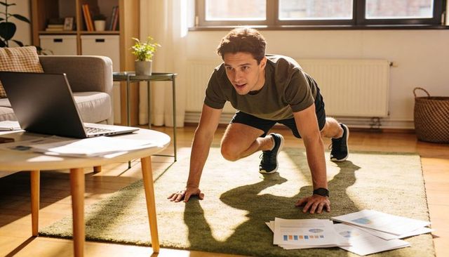 Young man performing intense home workout following live online fitness session on laptop
