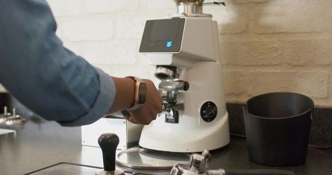 Preparing espresso using touchscreen grinder holding portafilter on minimal countertop