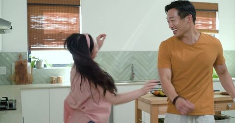 Playful couple dancing and laughing at sunlit modern kitchen island