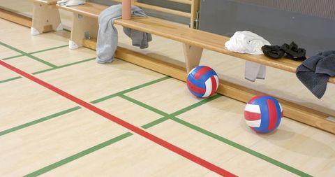 Wooden bench holding red white blue volleyballs and sportswear on indoor gym court lines