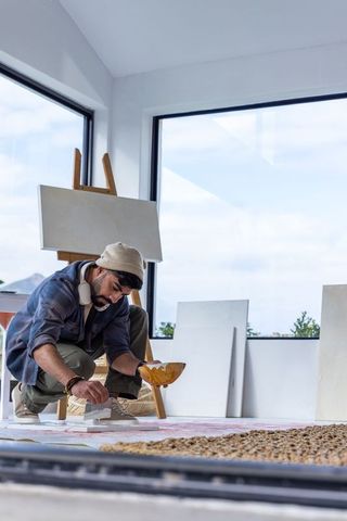Young male artist kneeling and painting floor canvas in bright modern minimalist studio