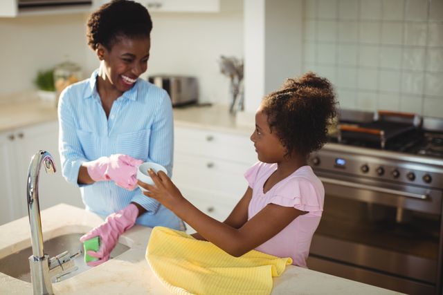 Mother assisting her daughter in cleaning utensils at home