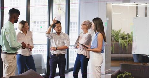 Diverse team brainstorming in modern office near glass wall using tablet and glass notes