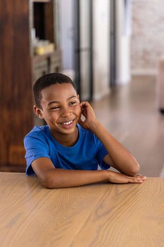African american boy smiling while leaning on wood table in bright kitchen