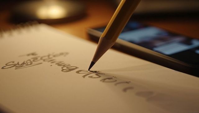 Pencil Writing Cursive Notes on Spiral Notebook with Warm Lamp Glow and Phone Blur