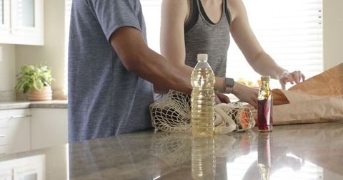 Couple unpacking groceries on glossy stone countertop with reusable bag and smartwatch