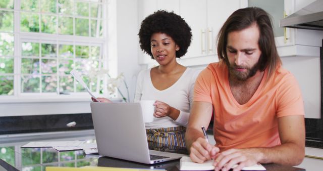 Happy biracial couple using laptop and calculating finances in the kitchen at home. staying at home in self isolation in quarantine lockdown