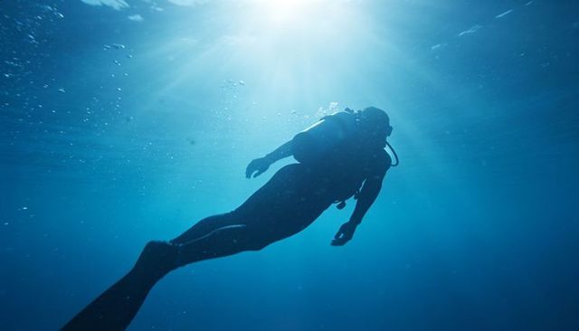 Silhouetted scuba diver gliding toward sunlit surface in deep blue water