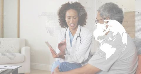 Woman doctor presenting tablet during home visit, showing telemedicine globe overlay