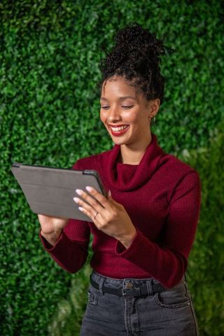 African american woman using tablet and smiling in front of lush green hedge wall
