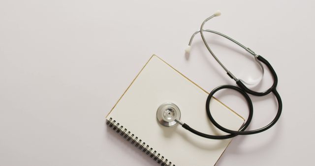 Image of close up of stethoscope with notebook on pink background. global medicine and healthcare concept.