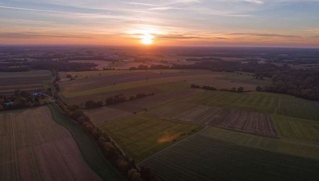 Hovering over golden patchwork farmland at sunset — evening countryside aerial view