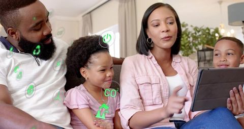 Black family sitting on couch using tablet together with floating eco tech icons