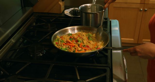 Woman preparing a healthy vegetable stir-fry in the kitchen. Fresh vegetables being sautéed in frying pan on stove. Ideal for features on home cooking, healthy eating, culinary skills, recipe blogs or online cooking courses.