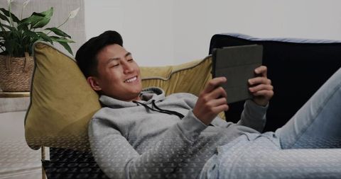 Relaxing Asian man using tablet on mustard sofa for home leisure and modern comfort