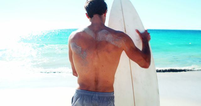 Rear view of man standing on beach with surfboard on a sunny day 4k