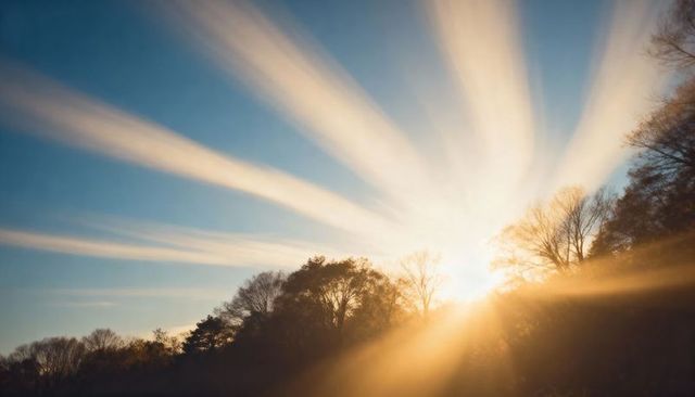 Sunburst rays bursting over woodland ridge at golden hour with warm sky beams