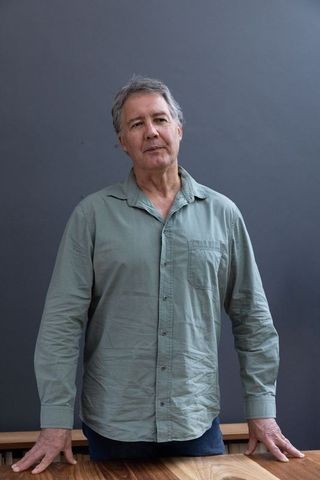 Mature Man in Light Green Shirt Contemplating Behind Wooden Table