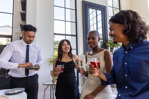 Diverse friends laughing and toasting with cocktails and appetizers in elegant lounge